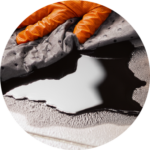 A hand wearing an orange glove using an absorbent pad to mop an oil leak