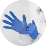 A person equipped with mask and coverall, putting on blue disposable gloves