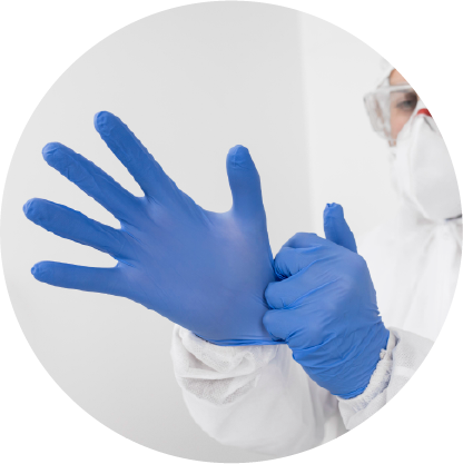A person equipped with mask and coverall, putting on blue disposable gloves