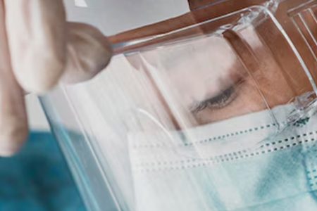 Healthcare worker wearing a face shield over a surgical mask and hairnet, representing Raxwell goggles and face shield supplies category
