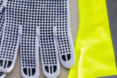 Close-up of white dotted knit work gloves laid on a high-visibility safety vest, illustrating Raxwell’s work gloves category